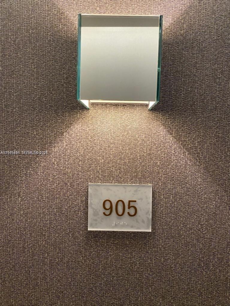 A wall-mounted light fixture illuminates a room number sign labeled 905 with braille — NORTH MIAMI BEACH, FL