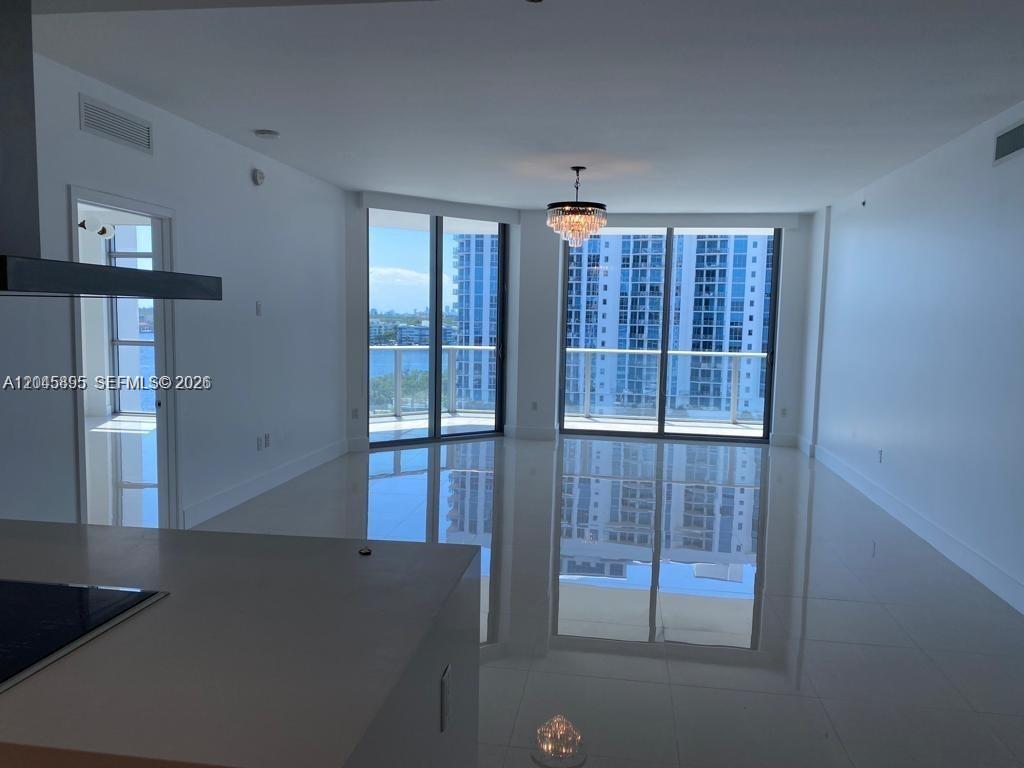 A modern, open-concept living area features white tile floors, a crystal chandelier, and floor-to-ceiling windows — NORTH MIAMI BEACH, FL