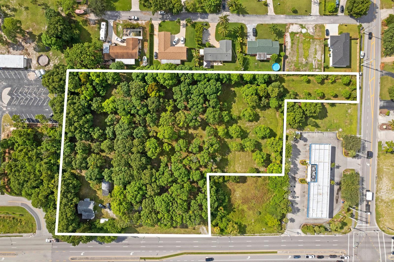 This aerial view shows a large, wooded lot outlined in white near a commercial building — 1908 Hypoluxo Road, Lake Worth FL 33462, LAKE WORTH, FL
