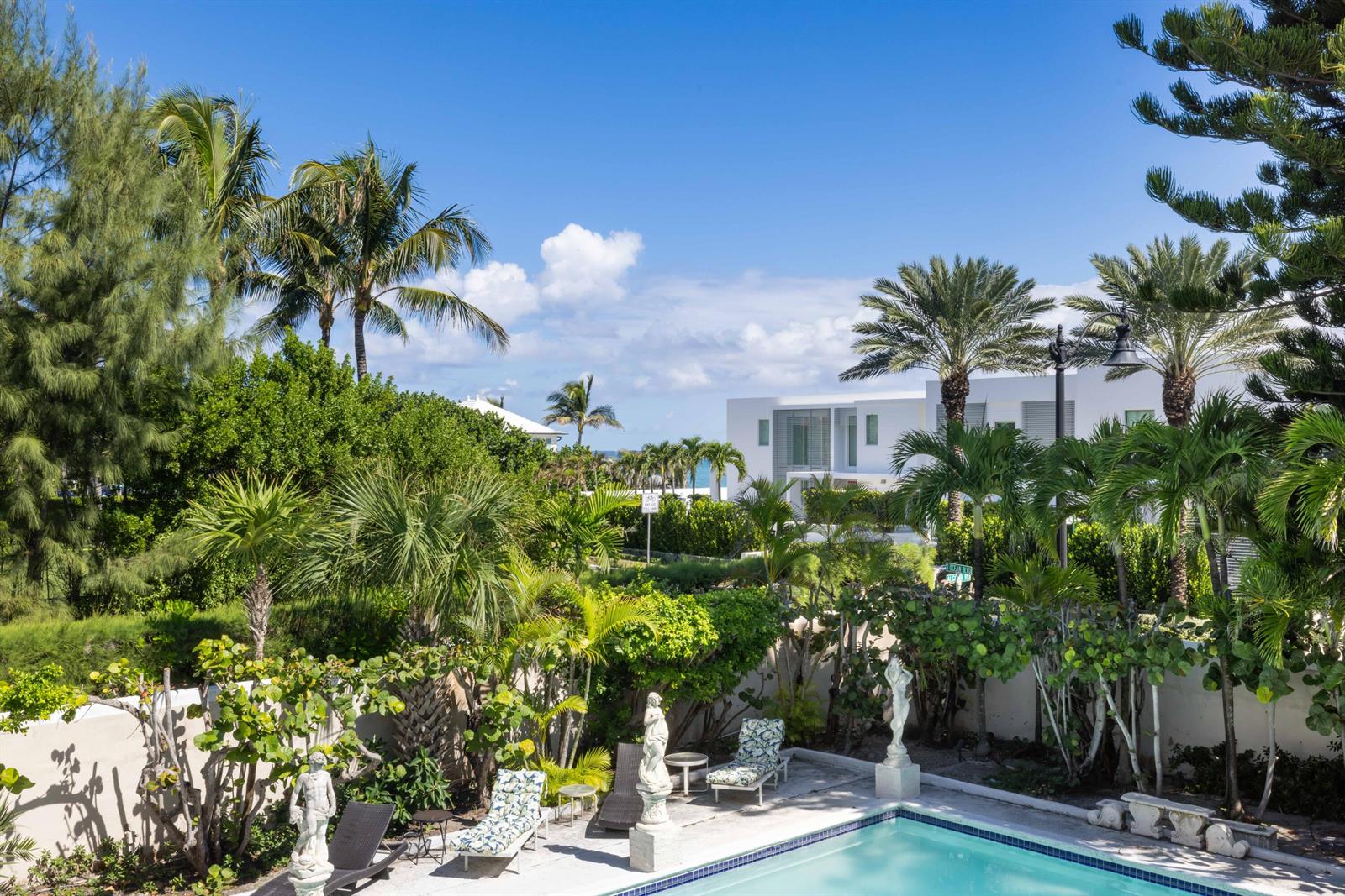 A swimming pool sits in a lush garden with palm trees and a modern house — 1048 S Ocean Boulevard, Palm Beach FL 33480, PALM BEACH, FL