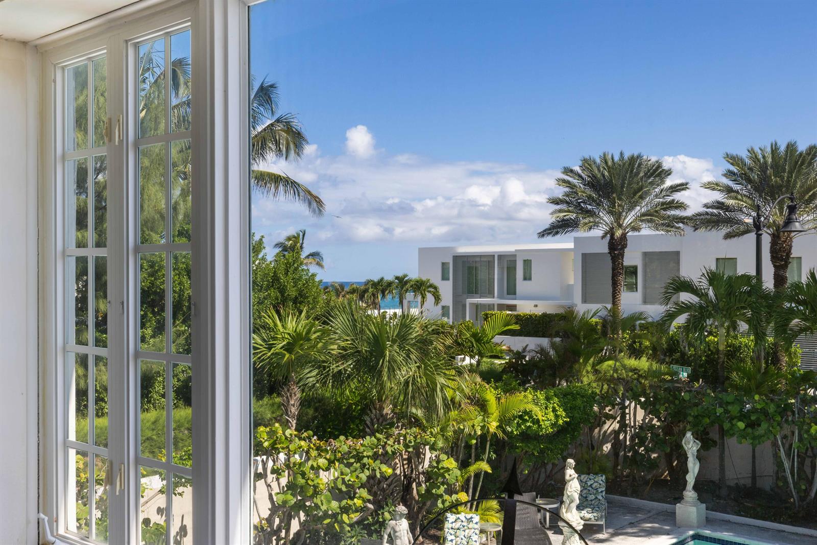 A view through a window shows a lush garden, palm trees, and a modern white house — 1048 S Ocean Boulevard, Palm Beach FL 33480, PALM BEACH, FL
