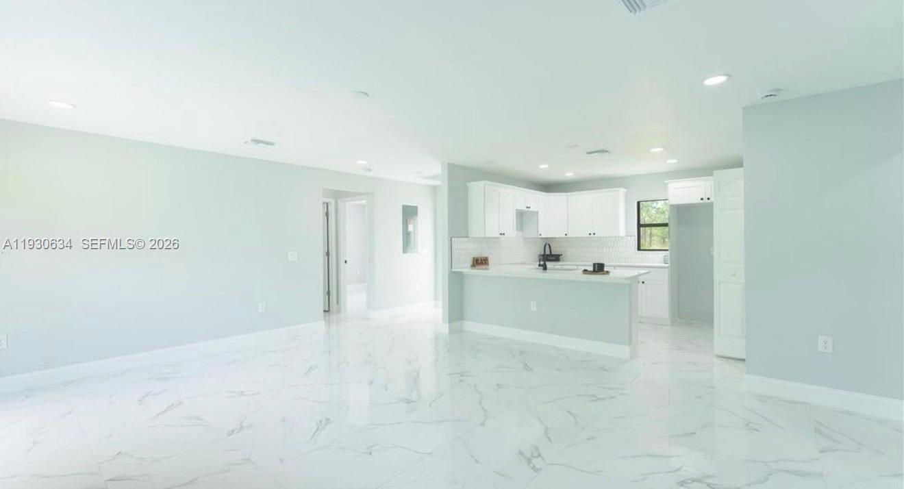 A bright, open-concept kitchen features white cabinetry, a marble-patterned floor, and a breakfast bar — 761 Kirkman Ave # 0, Lehigh Acres FL 33074, LEHIGH ACRES, FL