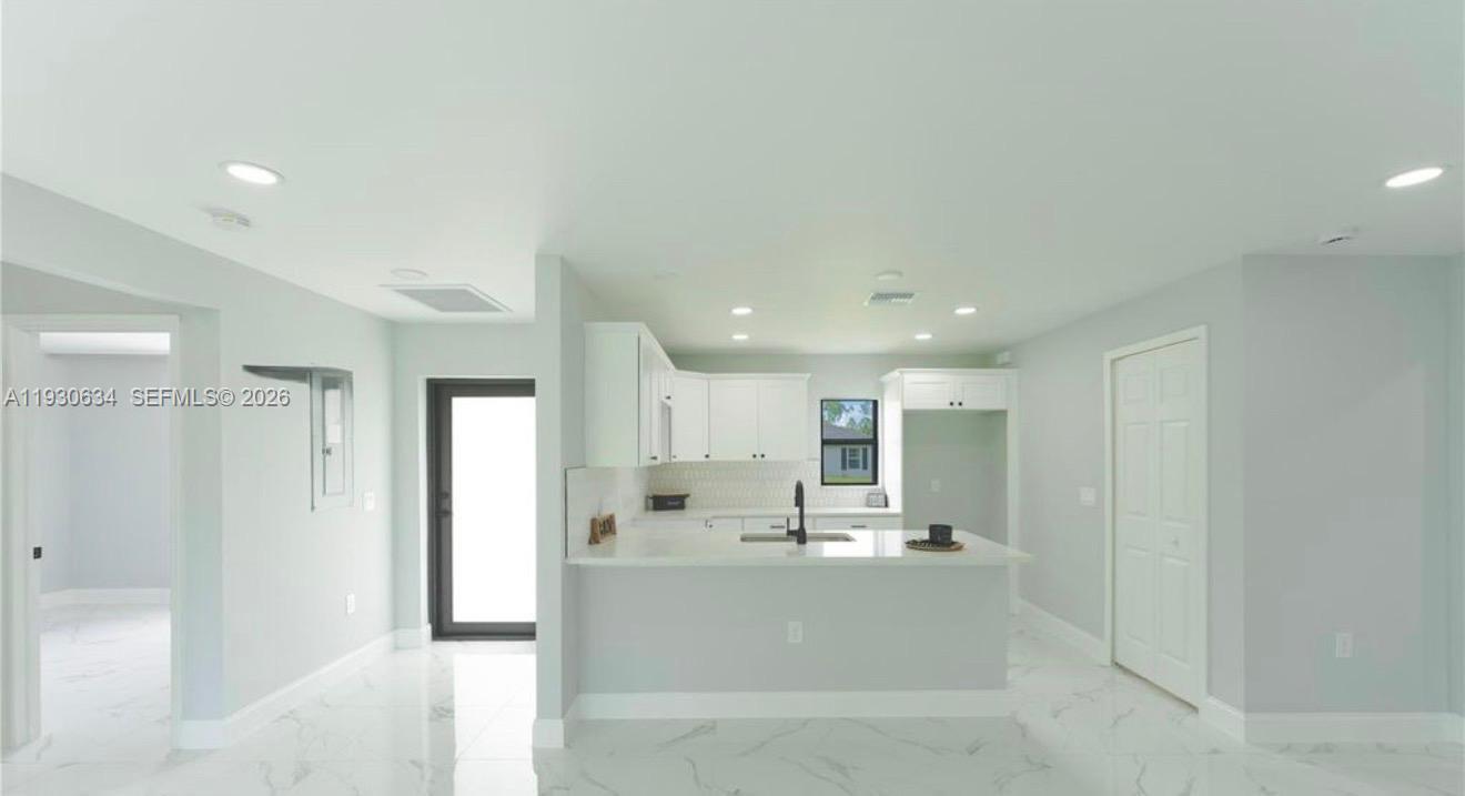 A modern kitchen features white cabinetry, a central island, and light-colored marble-style flooring — 761 Kirkman Ave # 0, Lehigh Acres FL 33074, LEHIGH ACRES, FL
