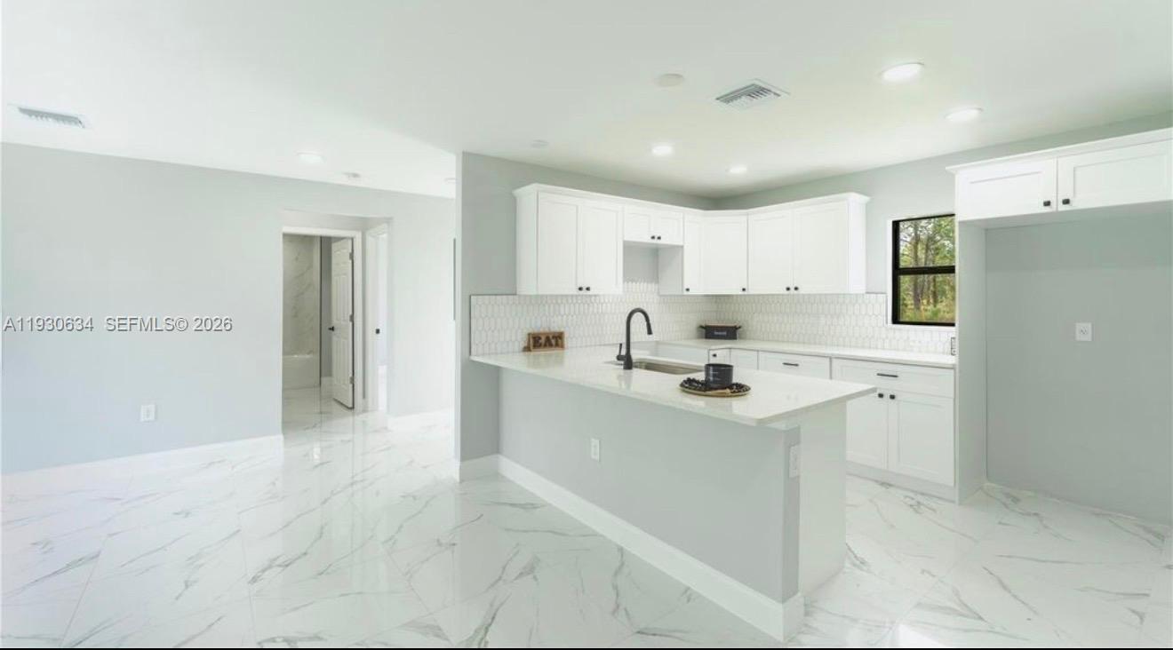A modern kitchen features white cabinets, a quartz island, and light-colored marble-patterned tile flooring — 761 Kirkman Ave # 0, Lehigh Acres FL 33074, LEHIGH ACRES, FL