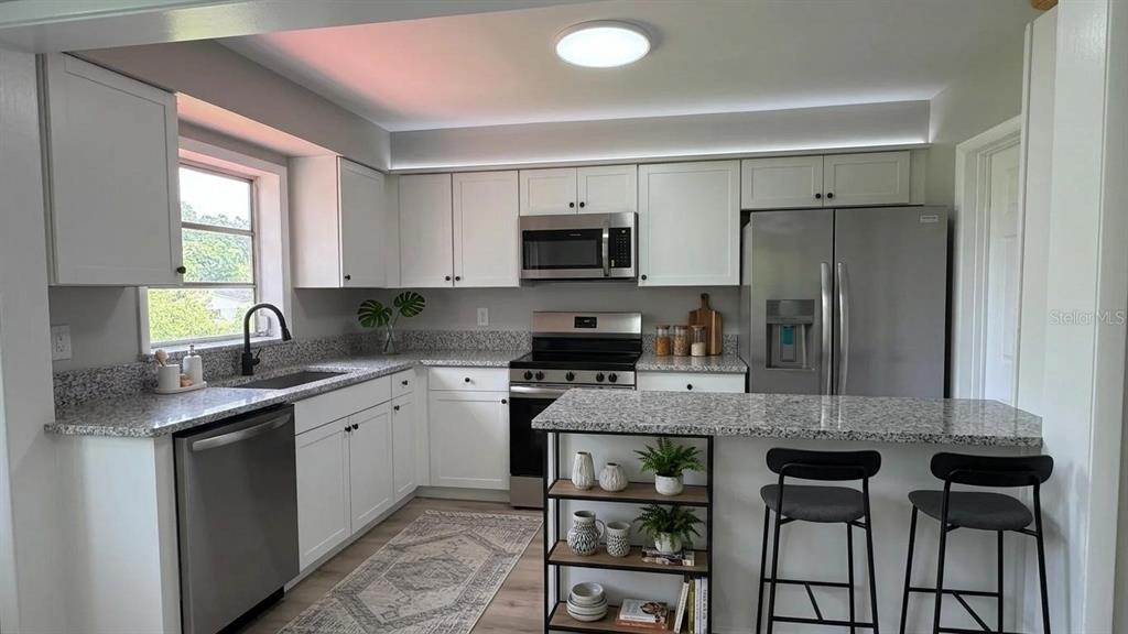 A kitchen features white cabinets, granite countertops, stainless steel appliances, and a breakfast bar with stools — 658 ELGROVE DRIVE, DELTONA, FL