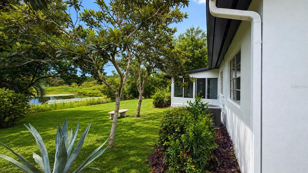 A white house exterior features a screened porch overlooking a grassy yard and a pond — 658 ELGROVE DRIVE, DELTONA, FL