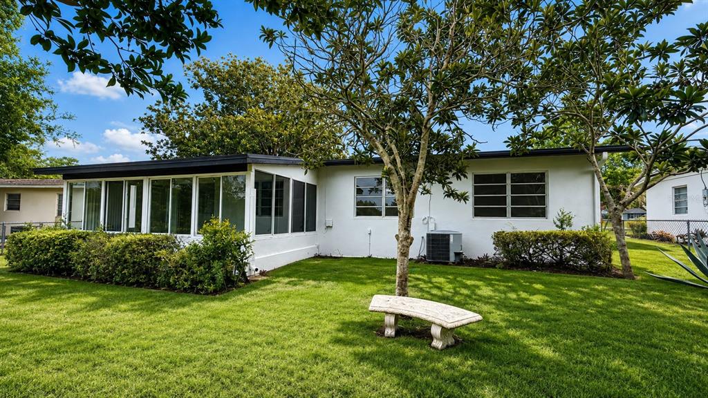 A white house with a sunroom and a stone bench on a grassy lawn — 658 ELGROVE DRIVE, DELTONA, FL
