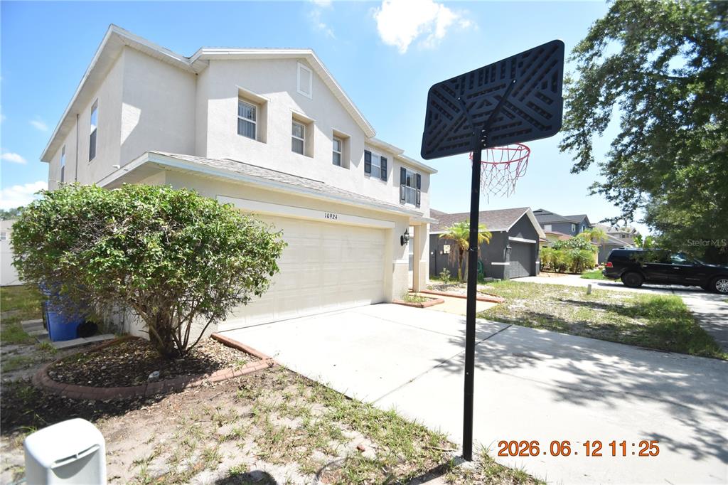 A two-story house with a beige stucco exterior, a two-car garage, and a basketball hoop — 10924 SUBTLE TRAIL DRIVE, RIVERVIEW, FL