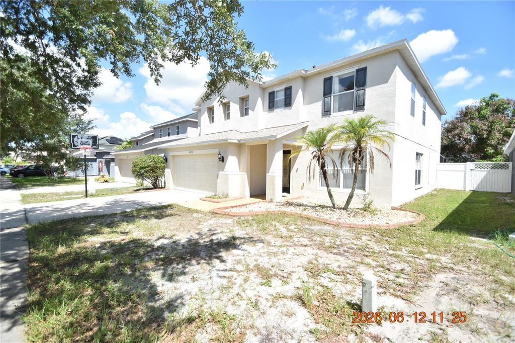A two-story suburban house with a beige stucco exterior, a two-car garage, and palm trees — 10924 SUBTLE TRAIL DRIVE, RIVERVIEW, FL