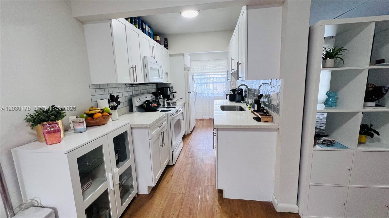 An open-concept living area features wood-look flooring, a small kitchen, and a window with curtains — 1100 NE 1st Ct # 213, Hallandale Beach FL 33009, HALLANDALE BEACH, FL