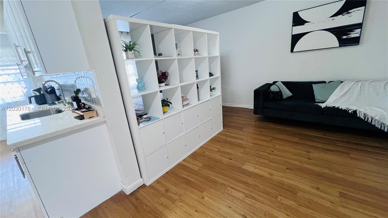 A living room features a gray sectional sofa, wood flooring, and a wall-mounted television — 1100 NE 1st Ct # 213, Hallandale Beach FL 33009, HALLANDALE BEACH, FL