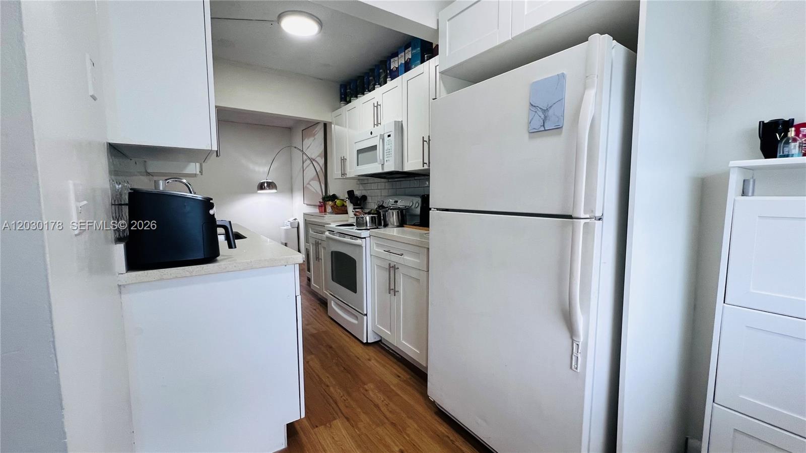 A galley kitchen features white cabinets, light countertops, and a window at the end — 1100 NE 1st Ct # 213, Hallandale Beach FL 33009, HALLANDALE BEACH, FL