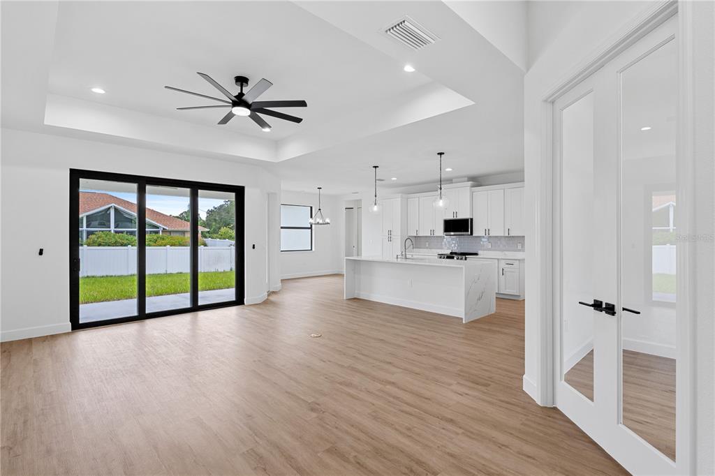 An open-concept kitchen and living area features light wood flooring, white cabinetry, and sliding doors — 2805 ANNISTON ROAD, NORTH PORT, FL
