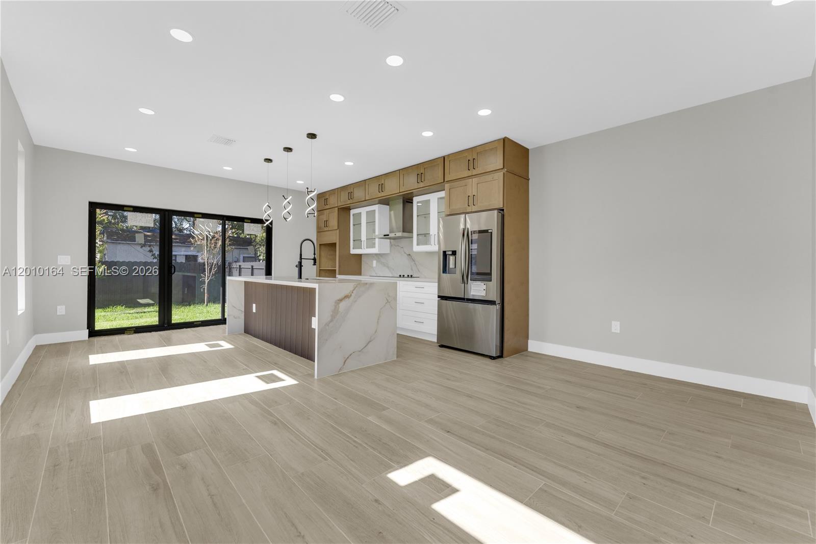A modern kitchen features a marble-topped island, wood-tone cabinetry, stainless steel appliances, and sliding doors — 1816 NW 49th St, Miami FL 33142, MIAMI, FL