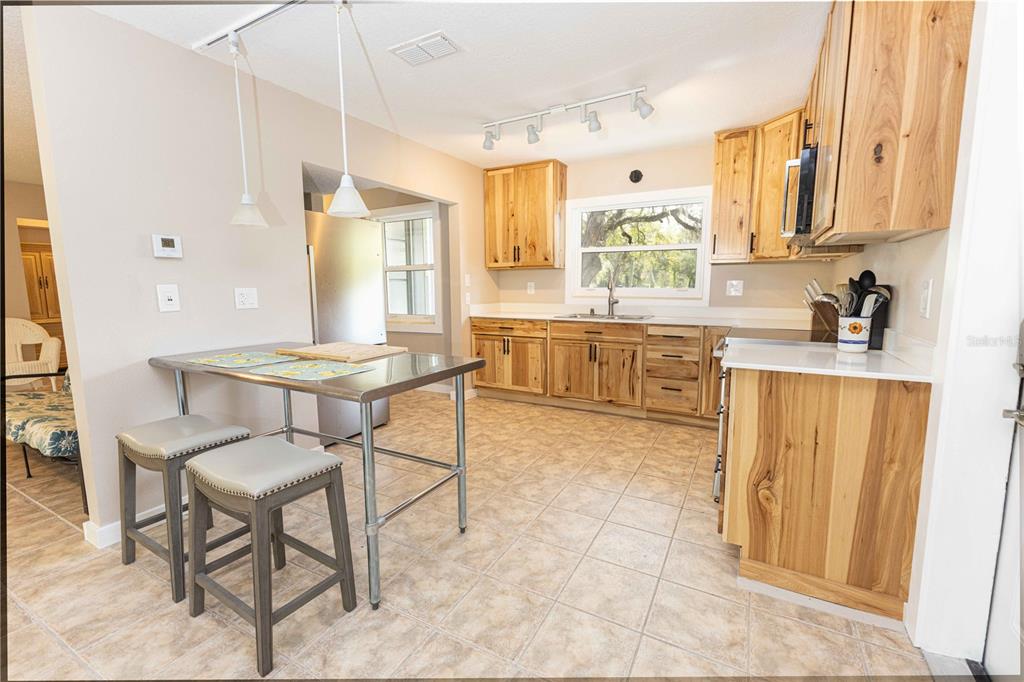 A kitchen with natural wood cabinets, stainless steel appliances, and a metal-topped dining table — 5175 AZALEA CIRCLE, DADE CITY, FL