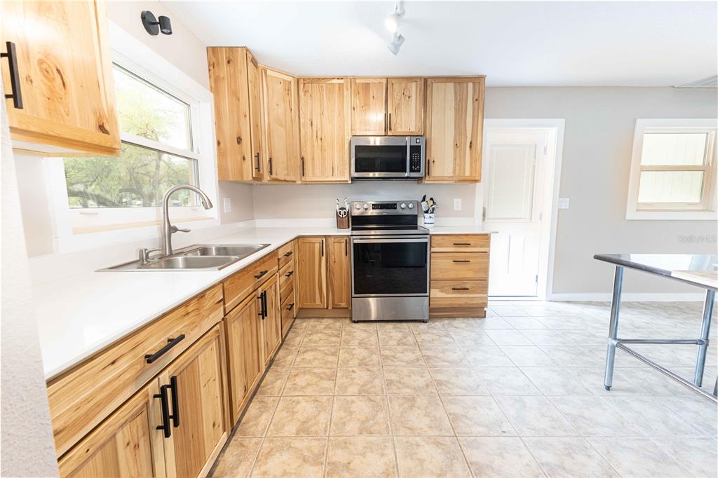 A kitchen features light wood cabinets, stainless steel appliances, white countertops, and tiled flooring — 5175 AZALEA CIRCLE, DADE CITY, FL