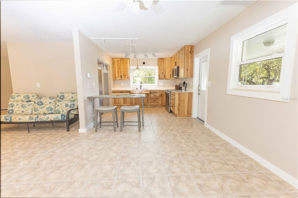 A kitchen and living area with light tile floors, wooden cabinets, and a floral sofa — 5175 AZALEA CIRCLE, DADE CITY, FL