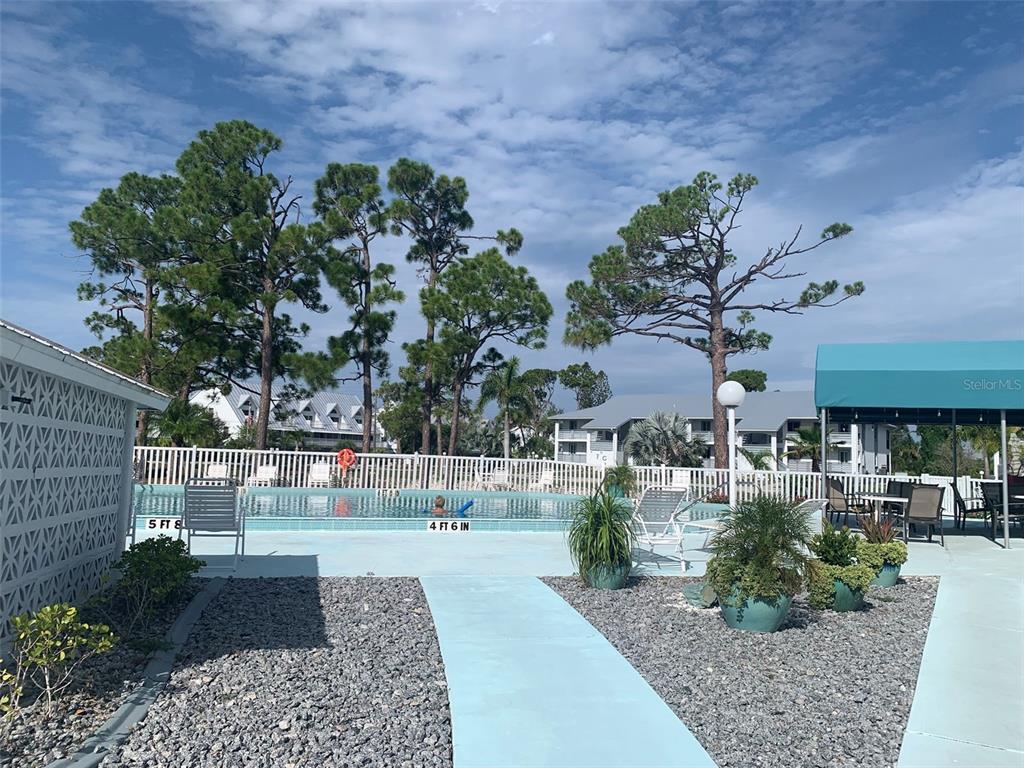 A swimming pool with depth markers is surrounded by a patio, landscaping, and apartment buildings — 6800 PLACIDA ROAD UNIT 2007, ENGLEWOOD, FL