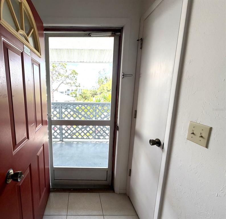 An open red front door reveals a tiled entryway with a white door and screen door — 6800 PLACIDA ROAD UNIT 2007, ENGLEWOOD, FL