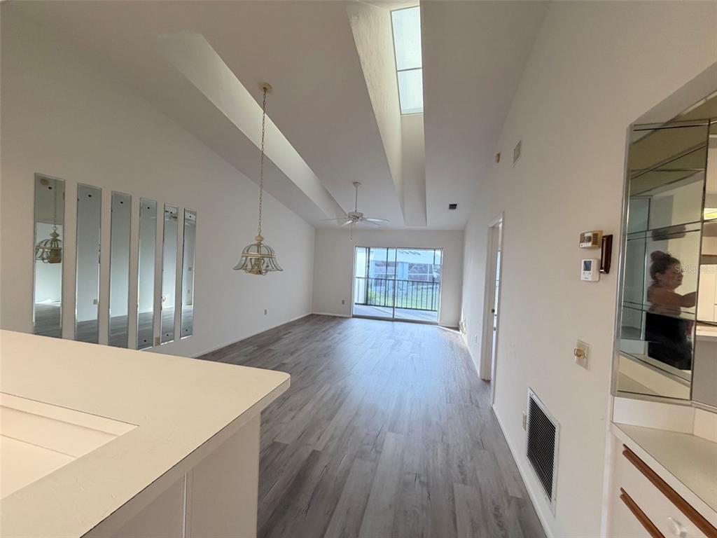 A living room with wood-look flooring, a vaulted ceiling with a skylight, and mirrored wall panels — 6800 PLACIDA ROAD UNIT 2007, ENGLEWOOD, FL