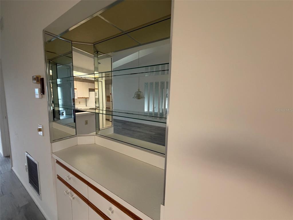 A built-in wet bar features mirrored walls, glass shelving, and white cabinetry — 6800 PLACIDA ROAD UNIT 2007, ENGLEWOOD, FL