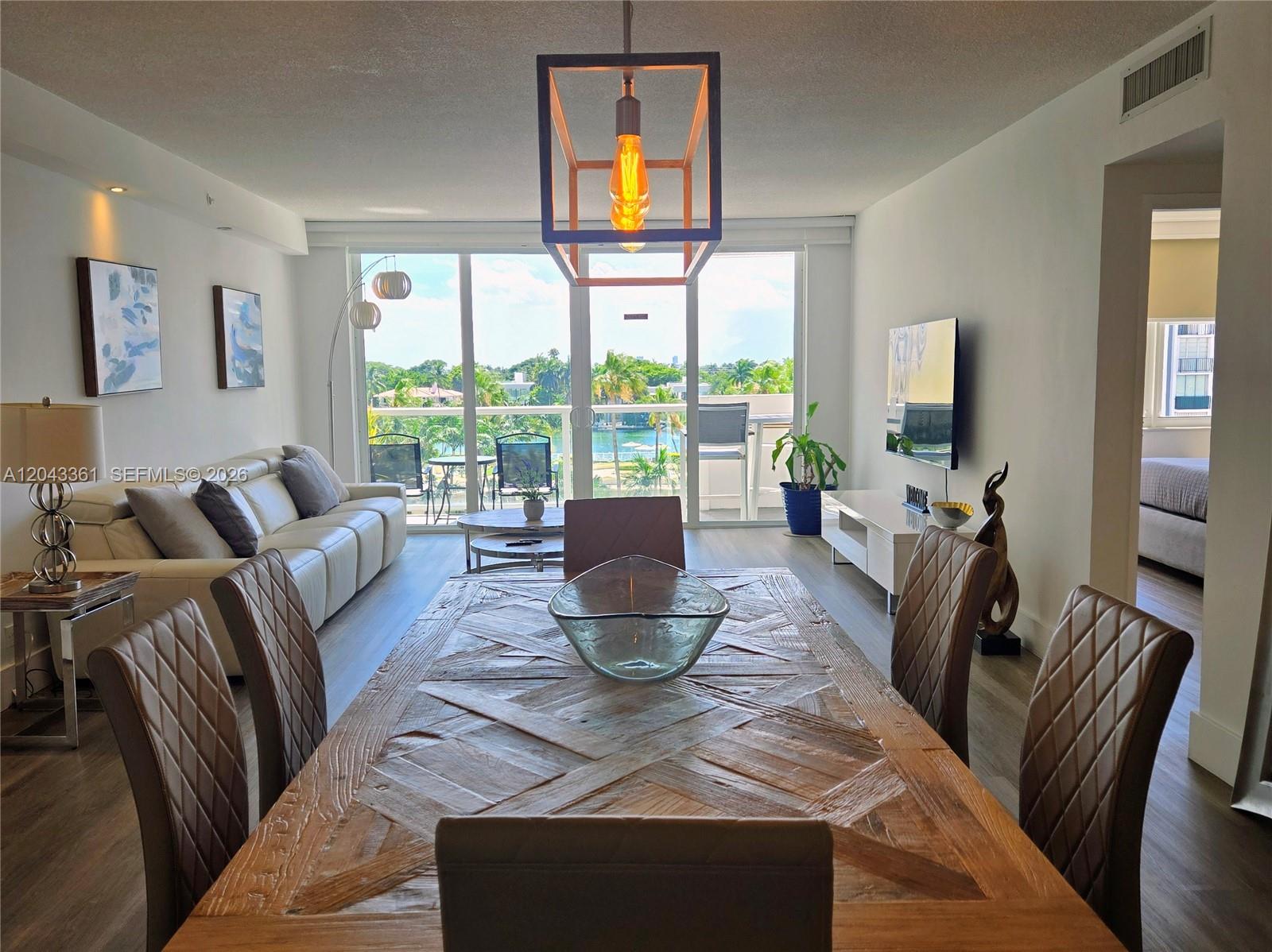 A dining area with a wooden table leads to a living room and balcony view — 5601 Collins Ave # 520, Miami Beach FL 33140, MIAMI BEACH, FL
