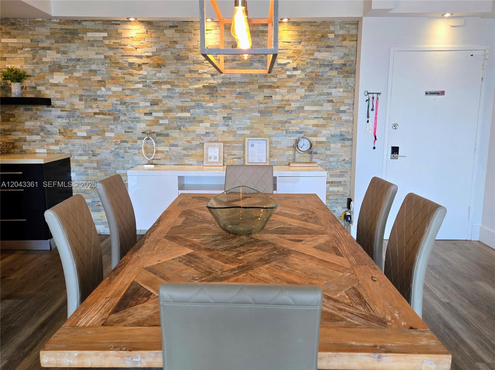A dining room features a wooden table, upholstered chairs, and a stone-tiled accent wall — 5601 Collins Ave # 520, Miami Beach FL 33140, MIAMI BEACH, FL