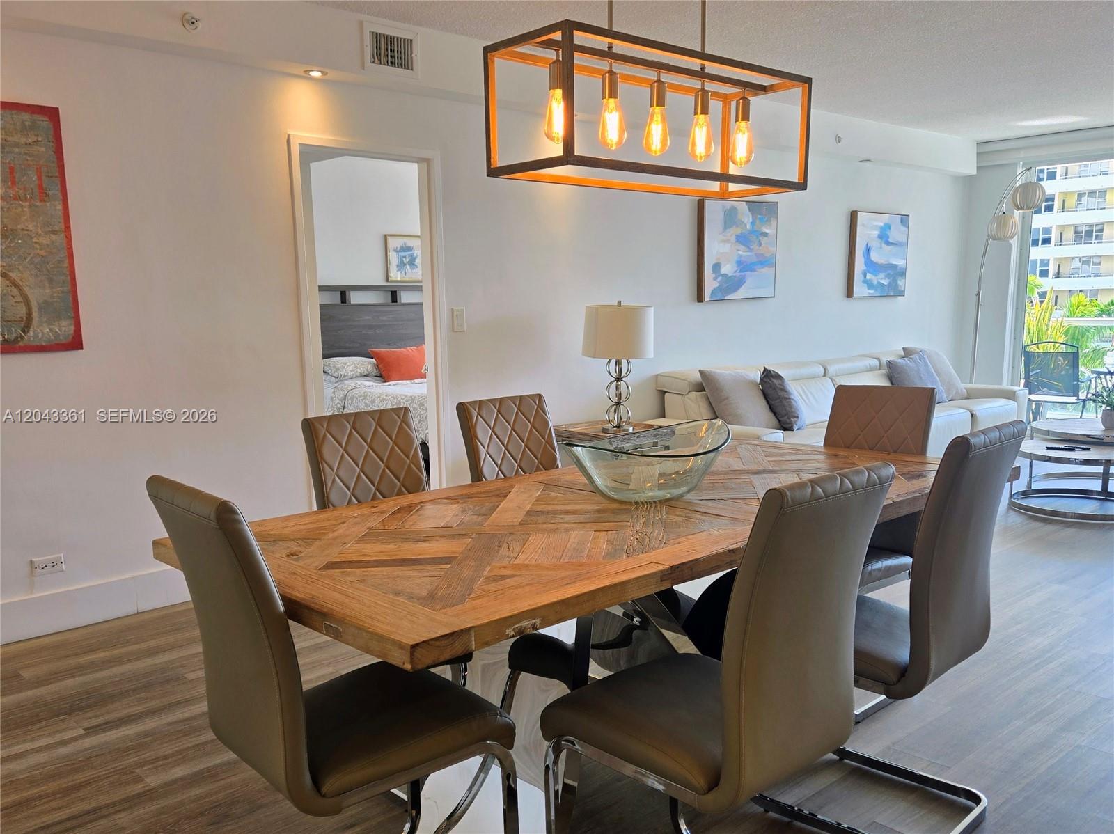 A dining area features a wooden table with six chairs under a rectangular pendant light — 5601 Collins Ave # 520, Miami Beach FL 33140, MIAMI BEACH, FL