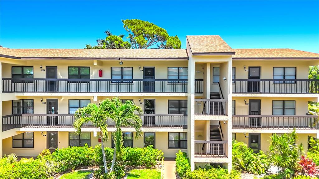 A three-story apartment building features beige stucco walls, dark railings, and a shingled roof — 425 30TH AVENUE W UNIT C212, BRADENTON, FL