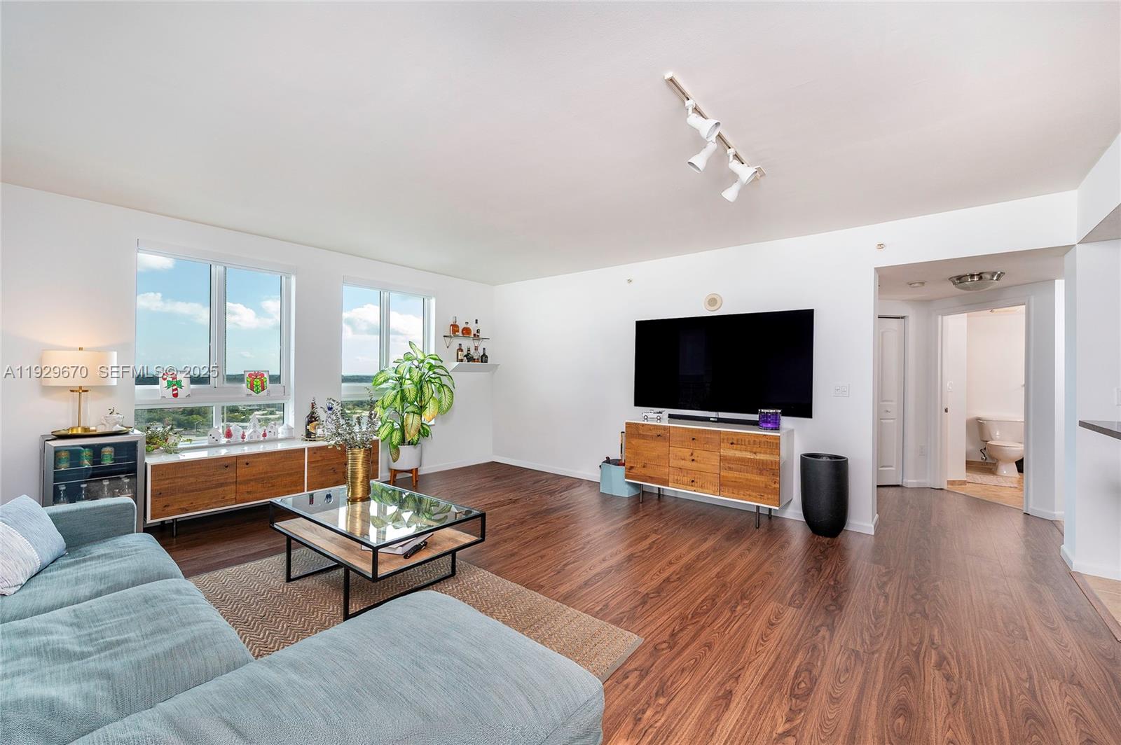 A living room features wood-look flooring, a blue sectional sofa, and a wall-mounted television — 7350 SW 89th St # 1702S, Miami FL 33156, MIAMI, FL