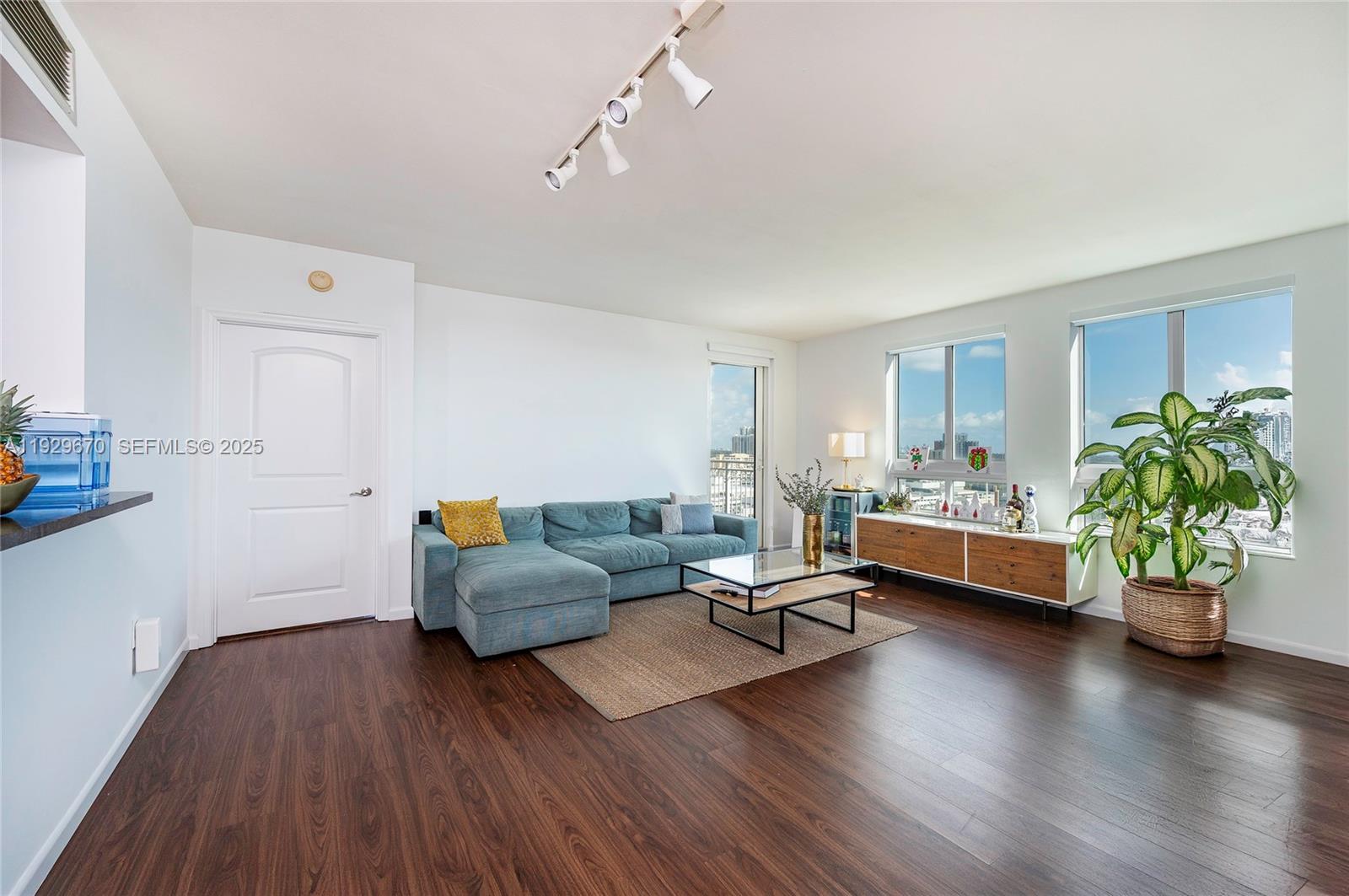 A living room features a blue sectional sofa, a glass coffee table, and wood flooring — 7350 SW 89th St # 1702S, Miami FL 33156, MIAMI, FL