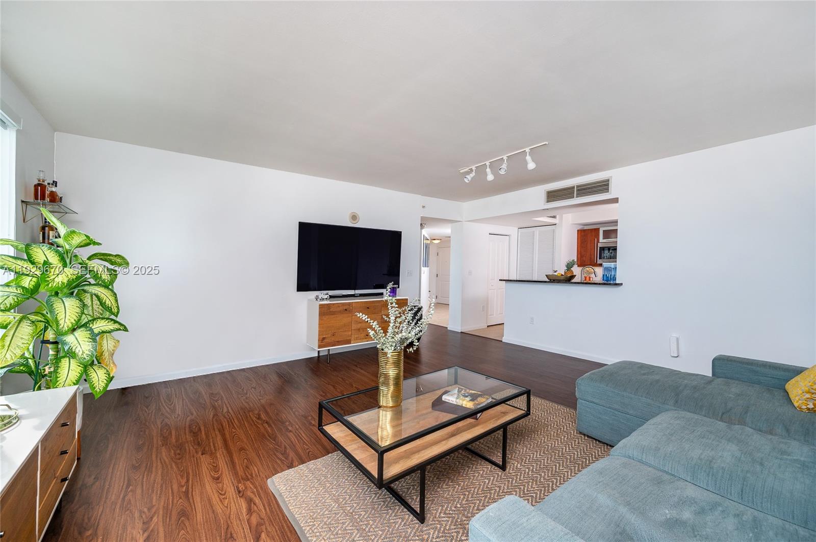 A living room features dark wood flooring, a blue sectional sofa, and a wall-mounted television — 7350 SW 89th St # 1702S, Miami FL 33156, MIAMI, FL