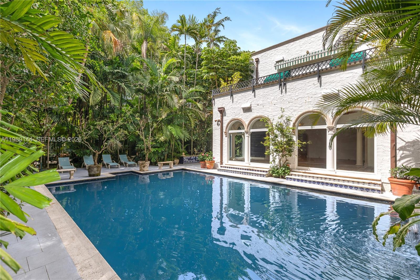 A swimming pool sits in front of a white stucco house with arched glass doors — 3685 Royal Palm Ave, Miami FL 33133, MIAMI, FL