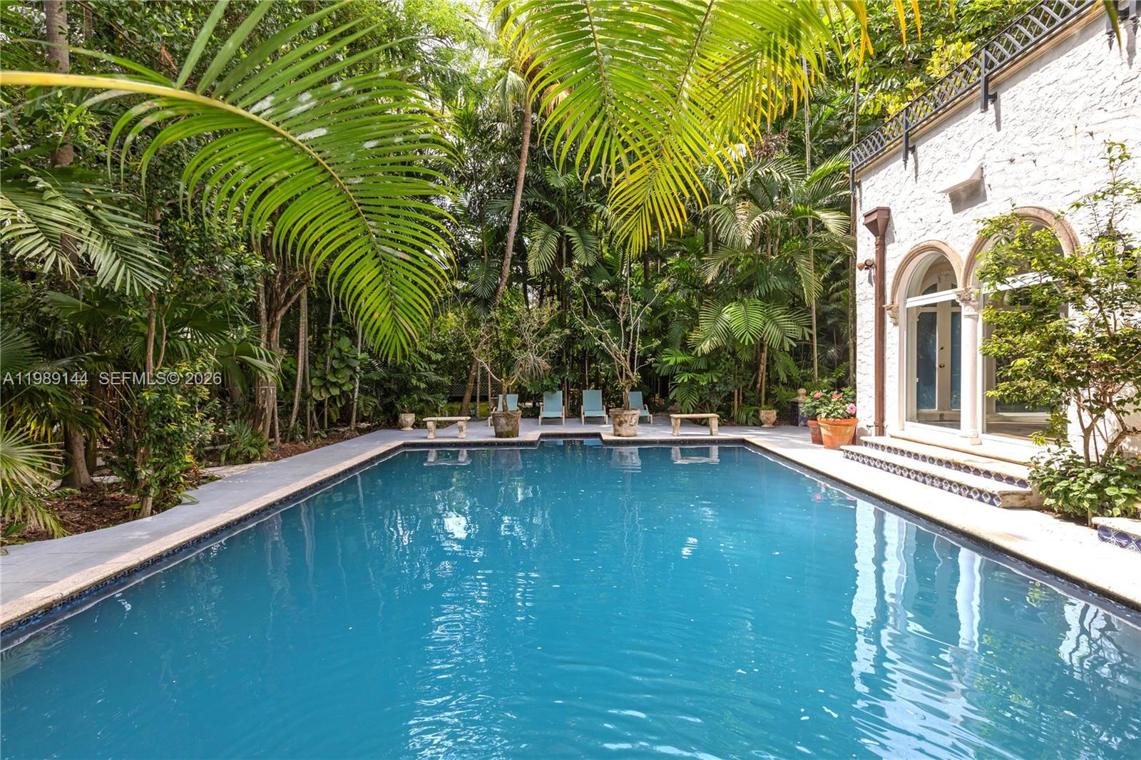 A rectangular swimming pool sits in a lush, tropical courtyard next to a white building — 3685 Royal Palm Ave, Miami FL 33133, MIAMI, FL
