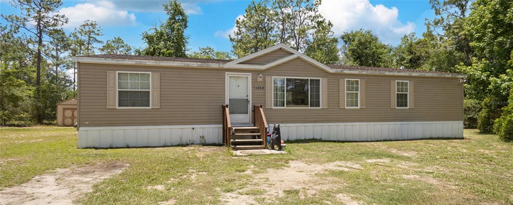 A tan manufactured home with white skirting sits on a grassy lot with trees — 14050 SE 20 STREET, MORRISTON, FL