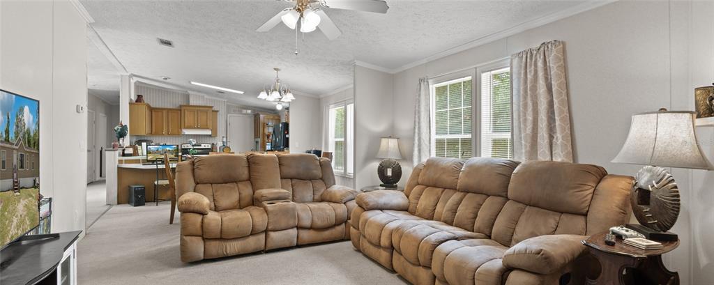A living room features two brown reclining sofas, beige carpeting, and an open kitchen area — 14050 SE 20 STREET, MORRISTON, FL