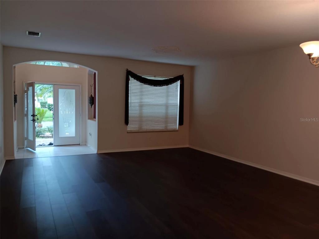 An open living area features dark wood flooring, a window with blinds, and an arched entryway — 10415 LUCAYA DRIVE, TAMPA, FL