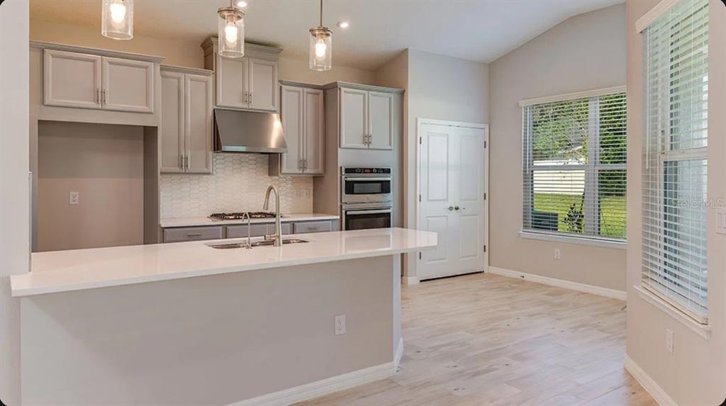 A modern kitchen features light gray cabinets, white countertops, stainless steel appliances, and wood flooring — 5769 BINNACLE LANE, COCOA, FL