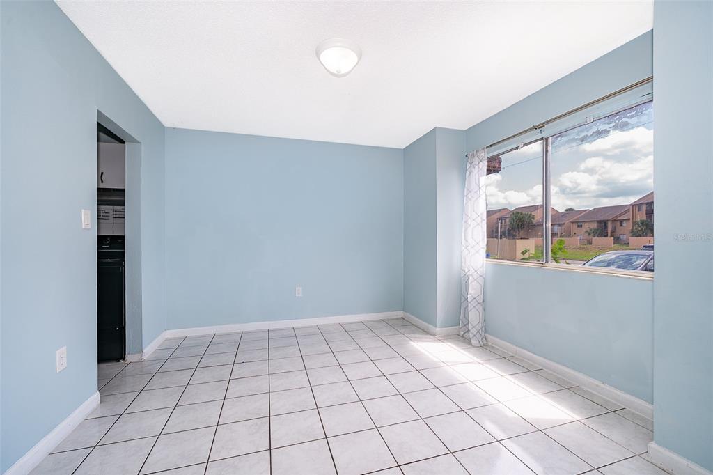 An empty room with light blue walls, white tile flooring, and a large window — 5060 DOWNING STREET UNIT 6, ORLANDO, FL