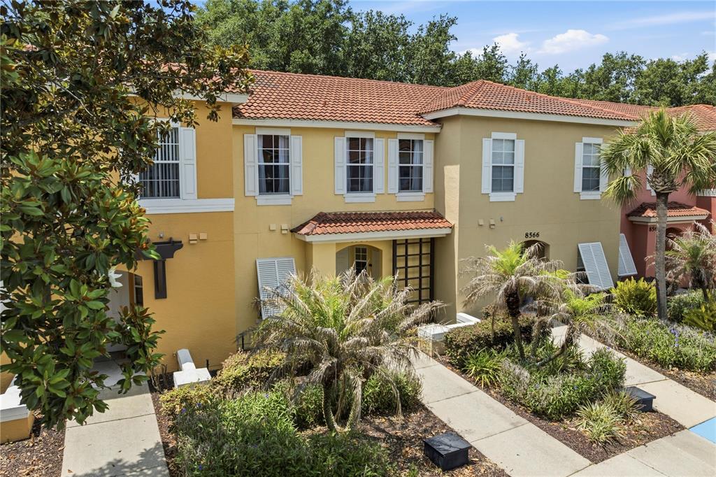 An exterior view of a two-story townhouse with yellow stucco walls and a tile roof — 8564 CRYSTAL COVE LOOP, KISSIMMEE, FL