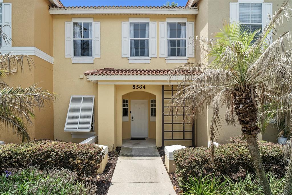 The exterior of a two-story yellow stucco townhouse features a front walkway and palm trees — 8564 CRYSTAL COVE LOOP, KISSIMMEE, FL
