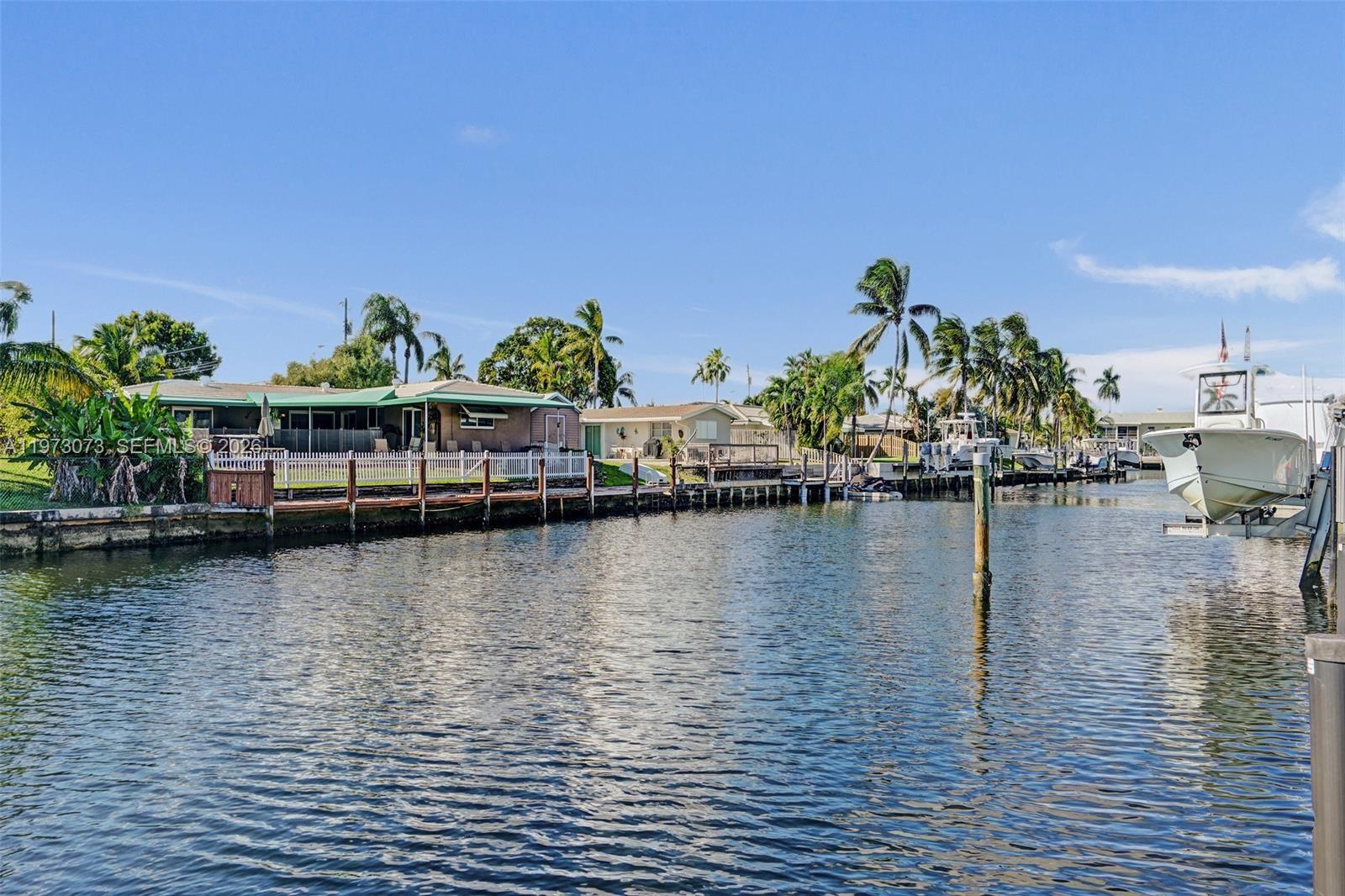 A waterfront view of houses with docks, palm trees, and a boat on a lift — 949 SE 10th Ct, Pompano Beach FL 33060, POMPANO BEACH, FL