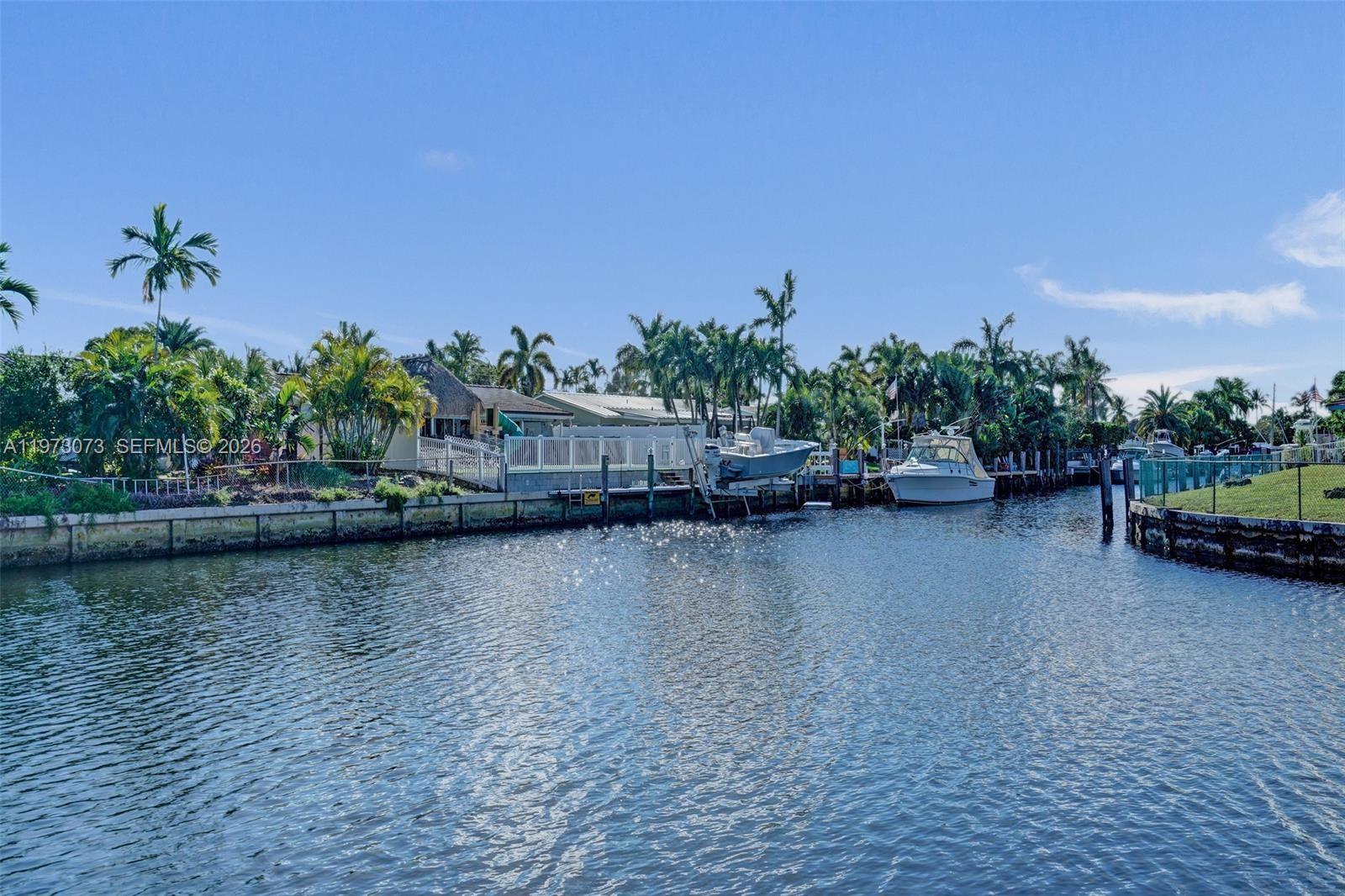 A canal view shows houses with docks, palm trees, and boats under a clear sky — 949 SE 10th Ct, Pompano Beach FL 33060, POMPANO BEACH, FL