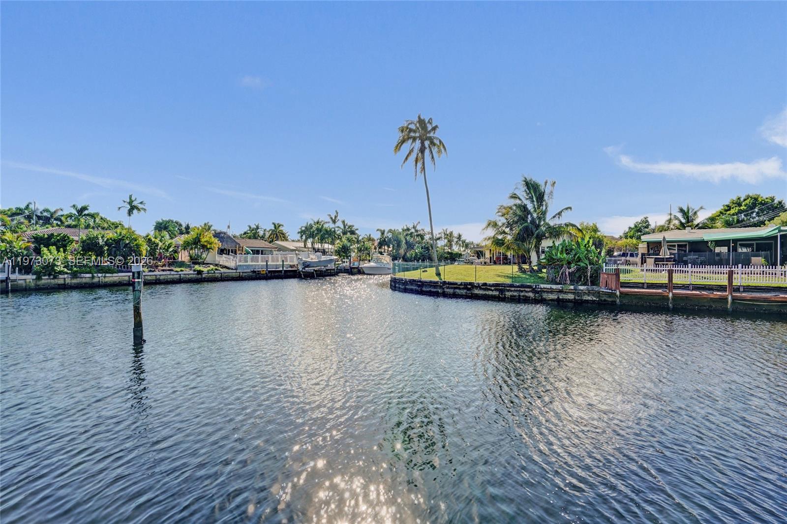 A view of a canal with houses, docks, and palm trees under a clear sky — 949 SE 10th Ct, Pompano Beach FL 33060, POMPANO BEACH, FL