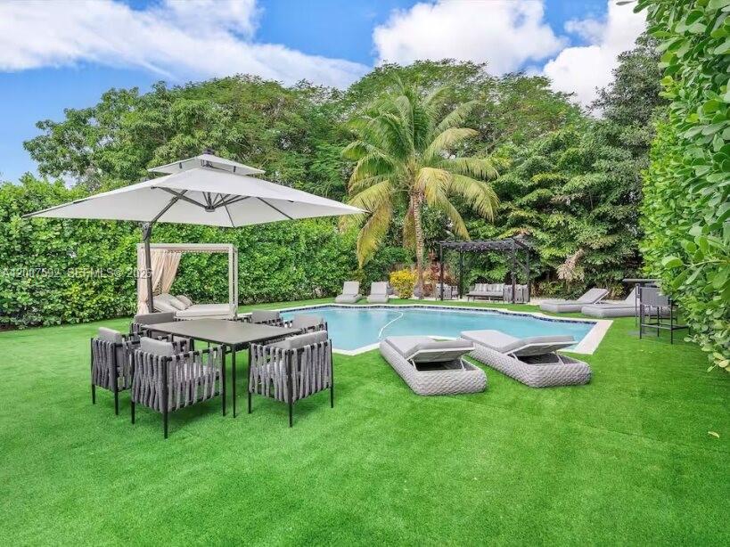 A backyard features a swimming pool, patio furniture, a large umbrella, and lush greenery — 545 NW 52nd St, Miami FL 33127, MIAMI, FL