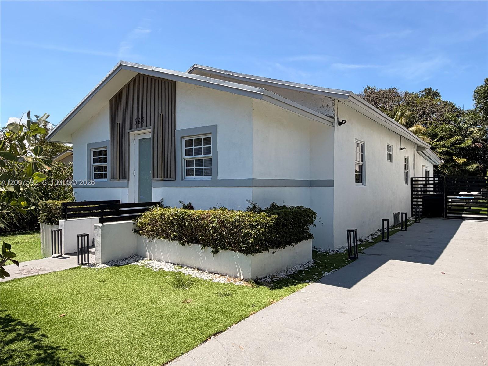 A white single-story house features a vertical wood accent wall, gray trim, and artificial turf — 545 NW 52nd St, Miami FL 33127, MIAMI, FL