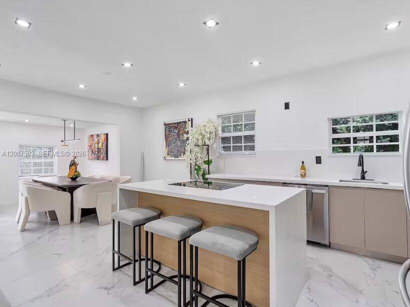 A modern kitchen features a white island with bar stools, light cabinetry, and marble flooring — 545 NW 52nd St, Miami FL 33127, MIAMI, FL