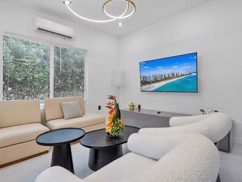 A modern living room features white walls, a curved sofa, and a wall-mounted television — 545 NW 52nd St, Miami FL 33127, MIAMI, FL