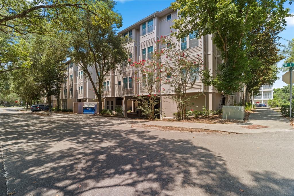 A multi-story apartment building with light-colored siding stands beside a paved street and trees — 835 SW 9TH STREET UNIT 101, GAINESVILLE, FL