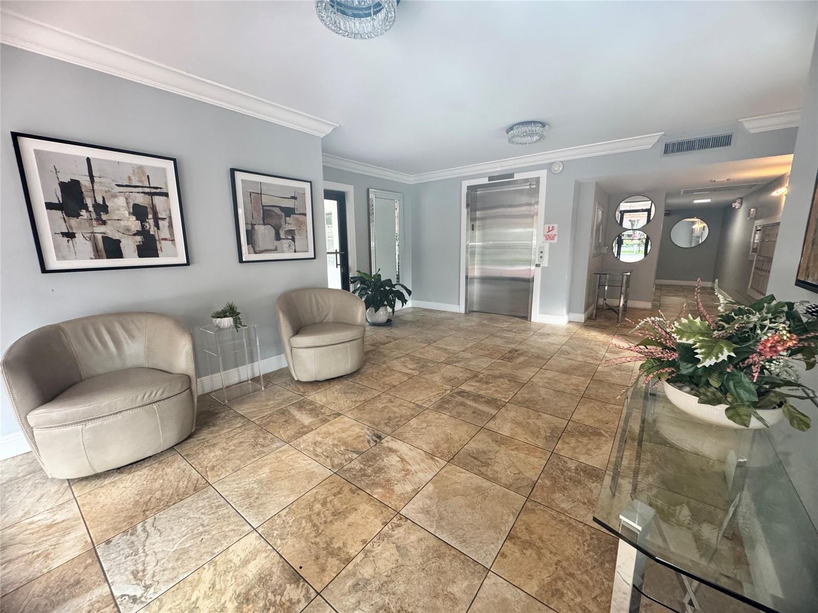 A lobby features beige tile flooring, two armchairs, abstract wall art, and a metal elevator — 2850 N Palm Aire Drive # 207, Pompano Beach FL 33069, POMPANO BEACH, FL